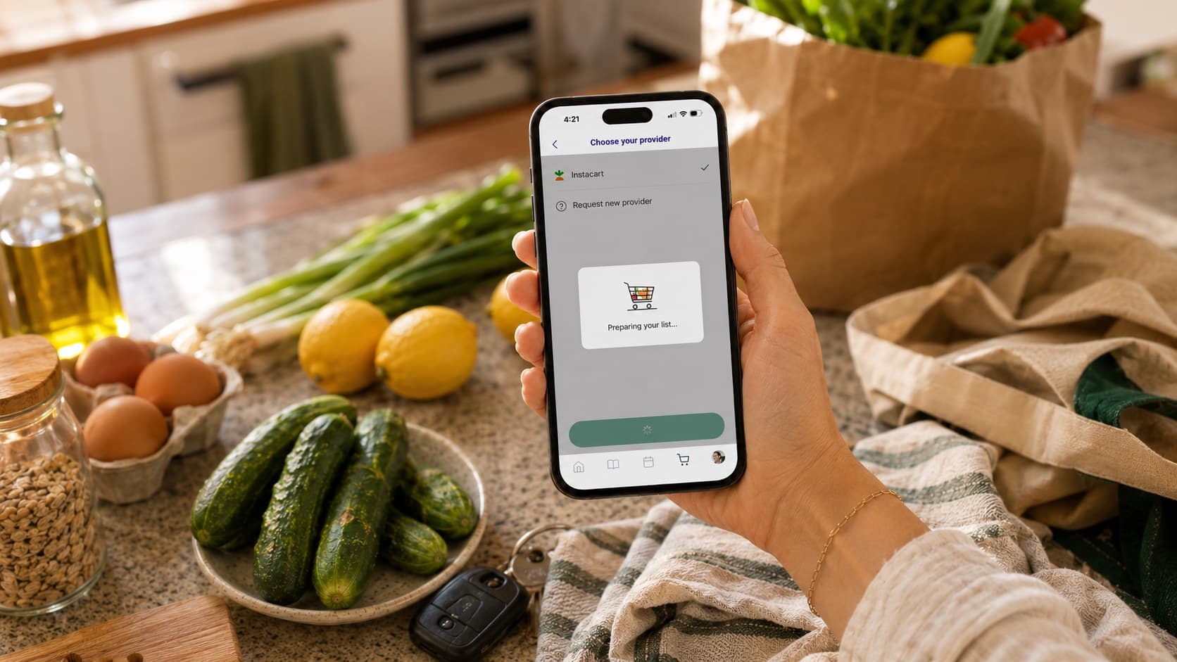 A hand holding an iPhone showing Deglaze's Choose your provider screen with Instacart selected and a "Preparing your list" card, over a kitchen counter with green onions, lemons, eggs, cucumbers, olive oil, and a paper bag of groceries.